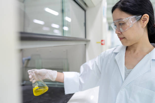 istock Scientist wearing a lab coat intently examines a yellow reagent flask while standing in front of a fume hood in a laboratory. The environment is equipped with advanced laboratory equipment, emphasizing the importance of precision and safety. 2158440978