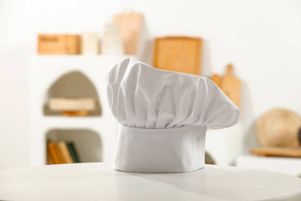Chef 's hat on counter table and white kitchen interior with blurred kitchen furniture. Space for products and objects. Cooking in bright kitchen.