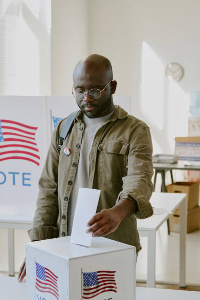 istock Young Black Man Placing Ballot Paper Into Box 2158441775