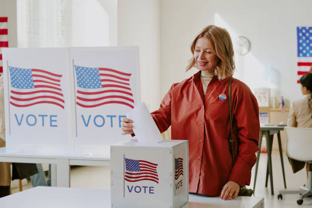 Modern senior Caucasian woman voting on election day placing ballot paper into box at polling station, copy space