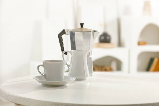 Coffee in a metal coffee maker on a white round table in a white modern dining room. Summer table background for montage product display or design key visual layout. View of copy space.
