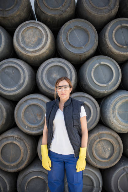 istock Worker woman with barrel background and work clothes. Protective glasses and gloves. Packaking factory 2158448677