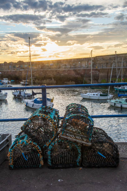 Picture of the harbour, crab creels on a shore, boats in a bay, dramatic skies of sunset behind the wall