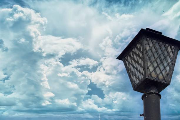 Interesting antique lantern on an iron pole with metal bars and glass, traditional shape, retro object, beautiful sky with a complex pattern of clouds, vintage background, daylight, stock photo, summer.