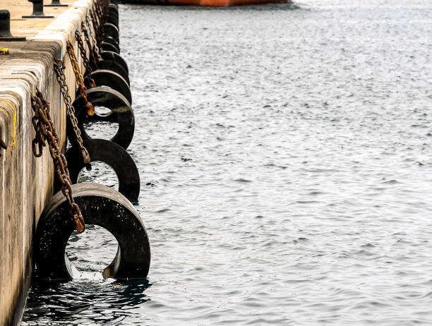 A row of tires are chained to a dock. The water is calm and the sky is overcast