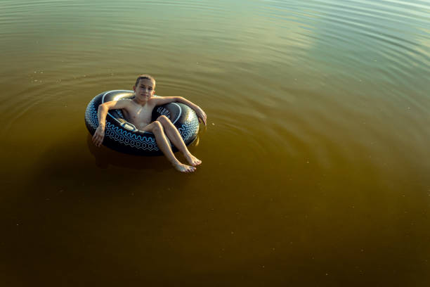 istock Boy enjoys a summer day at the lake with a rubber ring, looking at camera. 2158458150