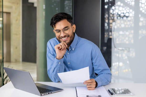 istock Smiling businessman reading document at desk with laptop and tablet 2158460208