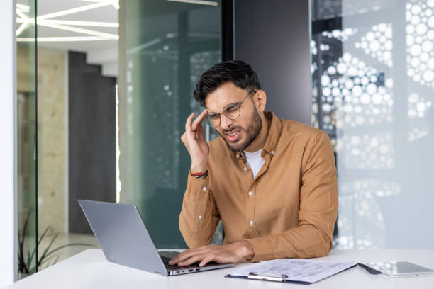 istock Frustrated man working on laptop at office desk with documents and tablet 2158462005