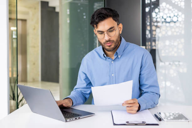 Focused businessman working on a laptop and reviewing documents in modern office