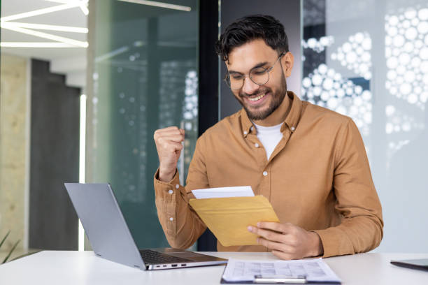 istock Excited young professional rejoices while reading letter at work desk 2158462881