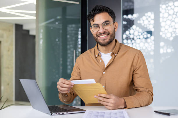 istock Smiling young businessman opening envelope at his desk in modern office 2158466459