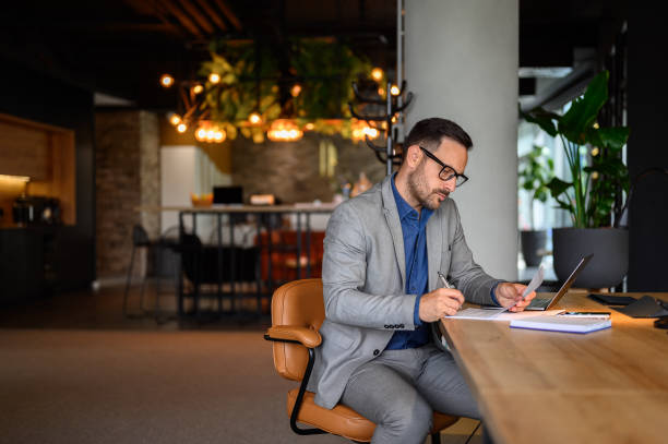 istock Serious male accountant with glasses examining spreadsheets and reports while sitting on chair at desk 2158469655