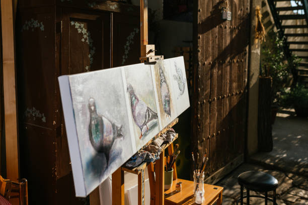 Creative paintings of doves on canvas placed on wooden easel in art studio on sunny day