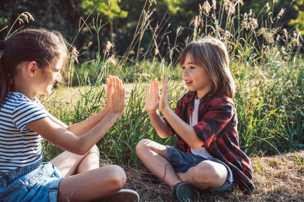 istock Kids play hand game in meadow, sitting amid tall grass happy 2158478910