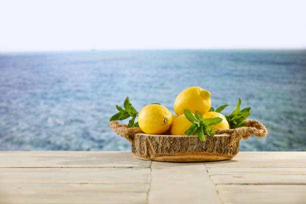 istock Yellow lemons scattered on wooden table top with blur  seascape background. 2158479457