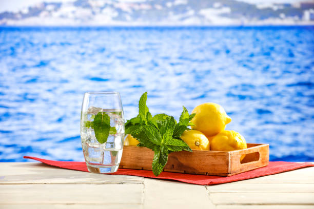 Photo composite of landscape and studio products: yellow lemons scattered on wooden table top and in the background a beautiful ocean and mountainous rocks and islands and clear sky.