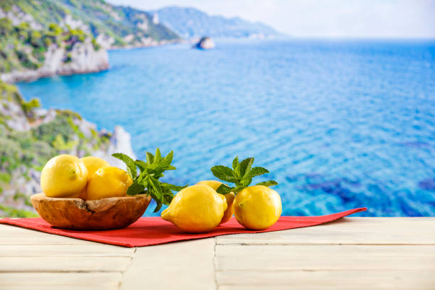 istock Yellow lemons scattered on wooden table top with blur  seascape background. 2158480230