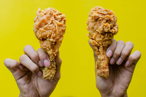 istock Hands holding fried chicken tigh isolated over yellow background 2158482154