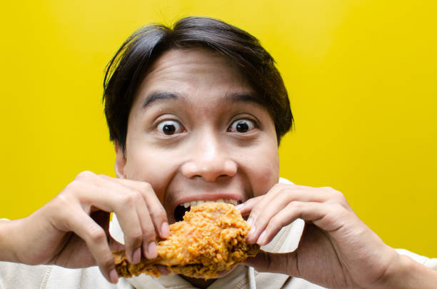 istock young asian man eats fried chicken drumstick with expression full of enjoyment 2158482664