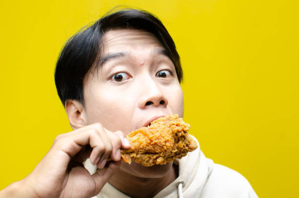 istock young asian man eats fried chicken drumstick with expression full of enjoyment 2158482756