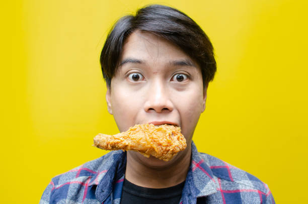 istock A funny, expressive Asian man holds a fried chicken drumstick with a wow expression isolated over a yellow background. 2158483202