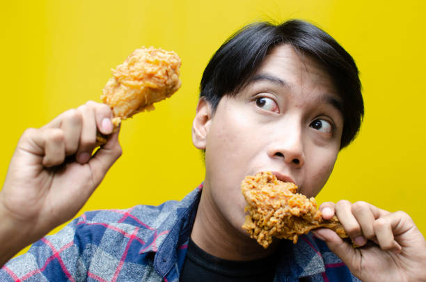 istock A funny, expressive Asian man holds a fried chicken drumstick with a wow expression isolated over a yellow background. 2158483292