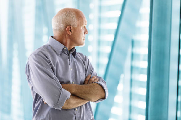 istock Senior businessman looking through office windows with arms cros 2158487242