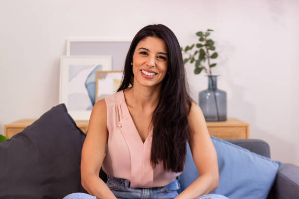 istock Young woman smiling while sitting on sofa at home in living room 2158487953