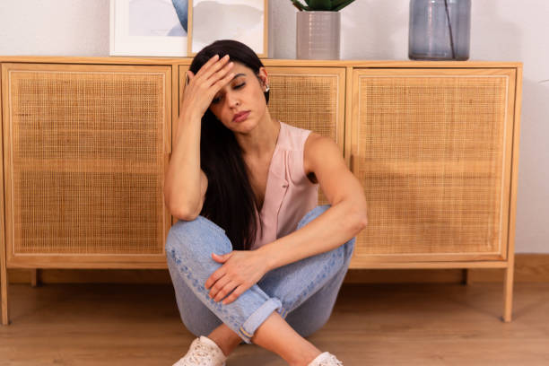 istock Sad woman sitting on floor touching her forehead feeling depressed 2158488632