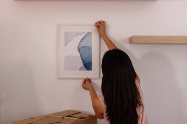 istock Young woman hanging a picture frame on a white wall 2158488665