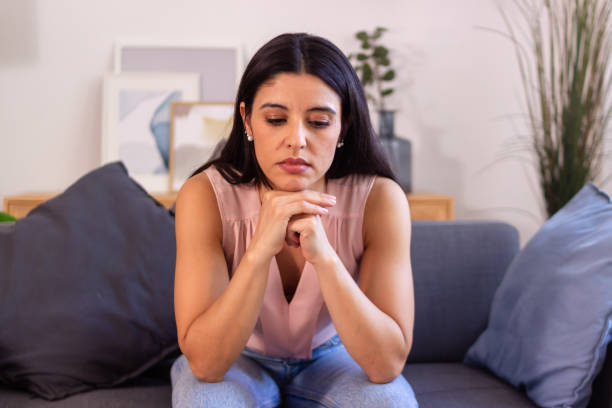 istock Young woman feeling sad sitting on sofa at home 2158489143