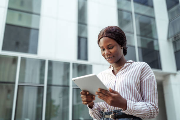 istock Young beautiful businesswoman using digital tablet while standing in front of modern business building 2158492525