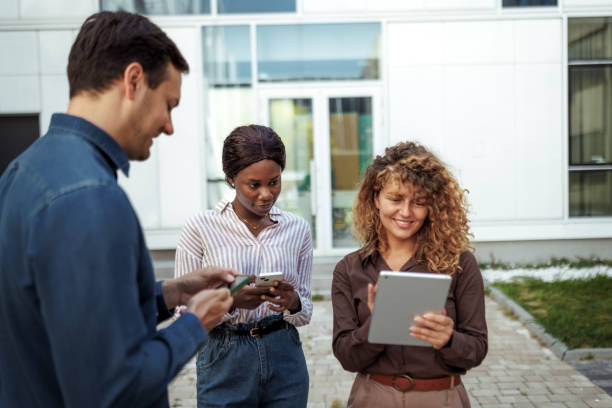 istock Three young colleagues using smart phone and digital tablet outdoors 2158492554