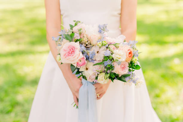 Bride is standing in a grassy field holding a pretty wedding bouquet.