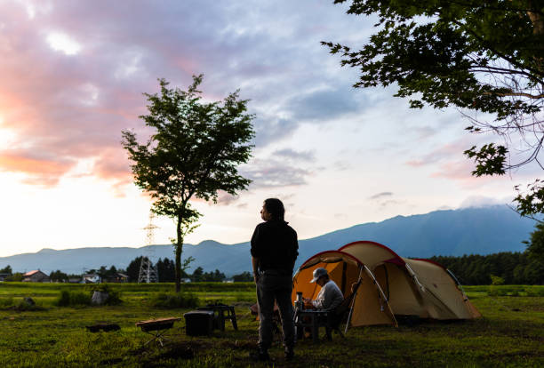 Two mid age friends camping enjoying the pink and purple colors of the sunset.