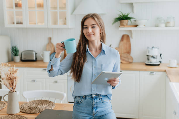 istock Woman holding a blue mug and tablet, smiling in a bright kitchen, enjoying her morning routine 2158522567