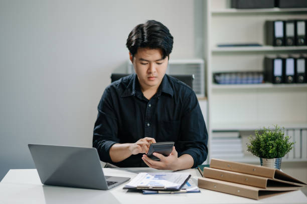 istock Young businessman working with working notepad, tablet and laptop documents talking on the smartphone, tablet and laptop 2158529354