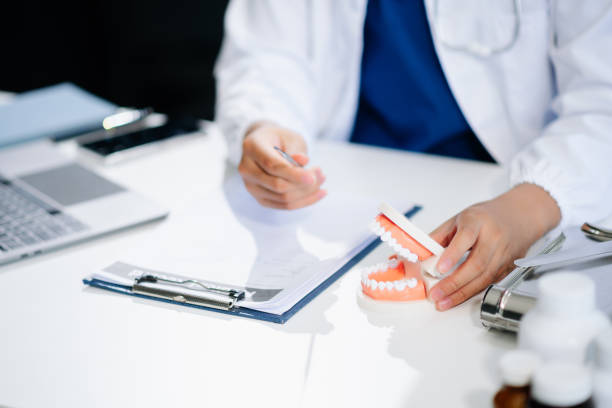 istock Dentist sitting at table with jaw samples tooth model and working with tablet and laptop. professional dental clinic. 2158529393