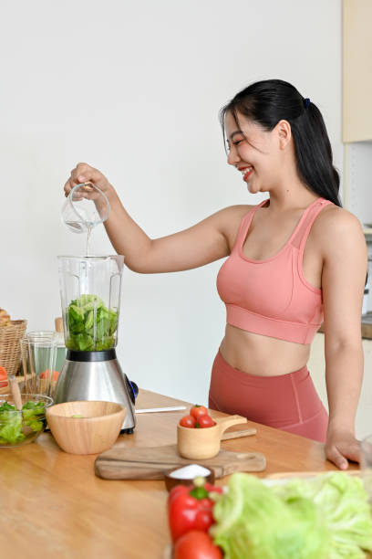 young woman making smoothie with fresh vegetables in kitchen.