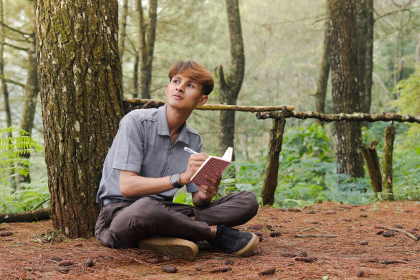 istock Portrait of confident Asian man writing on notebook while thinking and looking away in the nature forest. Peaceful and relaxing healthcare wellness 2158533537