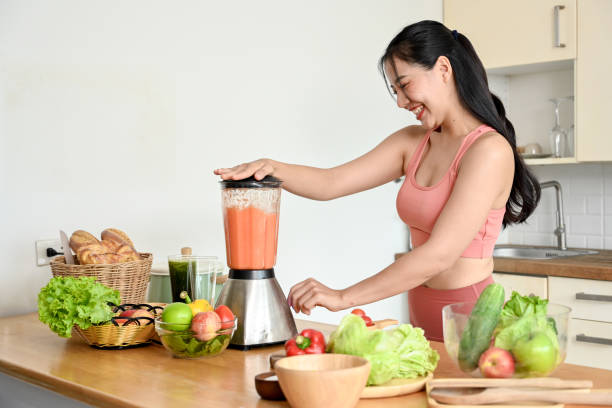 istock Smiling young woman making smoothie with fresh vegetables in kitchen. 2158533637