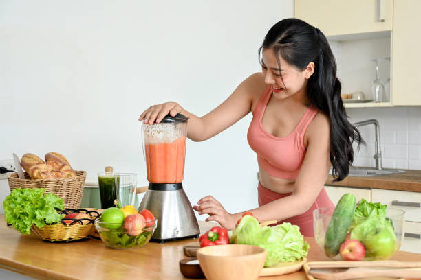 istock Smiling young woman making smoothie with fresh vegetables in kitchen. 2158533642