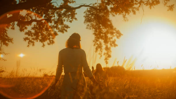 A woman and young girl, likely family, enjoy a peaceful swing ride under a solitary tree bathed in the glow of a golden sunset, symbolizing quality time and the simplicity of nature's backdrop.