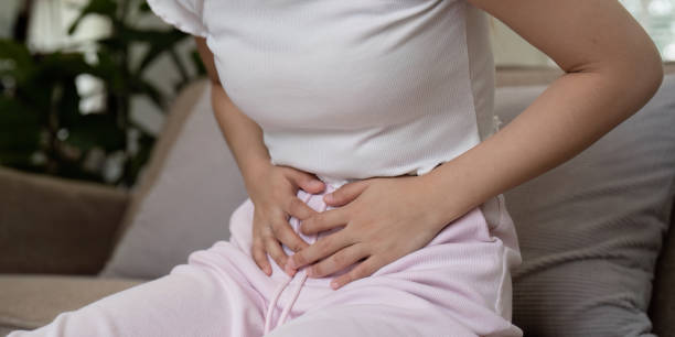 istock Woman Experiencing Stomach Pain While Sitting on a Couch in a Home Setting, Clutching Her Abdomen in Discomfort 2158542339