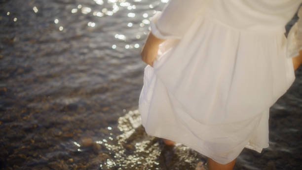 A mature Caucasian lady finds serenity standing in a gentle river, her flowing dress mirroring the water's calm, reflecting a moment of relaxation in nature.