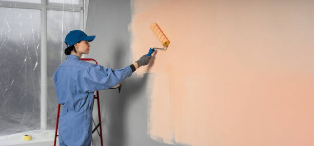 istock Side view of painter woman painting the wall, with paint roller on empty space for text 2158544692