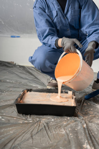 Woman pours paint into the tray. Professional interior construction worker or decorator pouring paint to tray.
