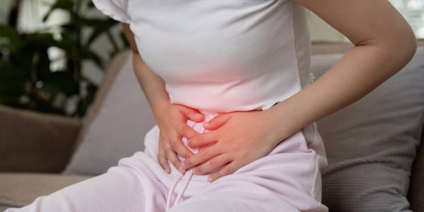 istock Woman Experiencing Stomach Pain While Sitting on a Couch in a Home Setting, Clutching Her Abdomen in Discomfort 2158545339