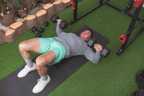 istock A fit asian man in a gray sweater does dumbbell floor presses with hip bridge. Shoulder friendly workout and upper chest training at his home gym. 2158547347