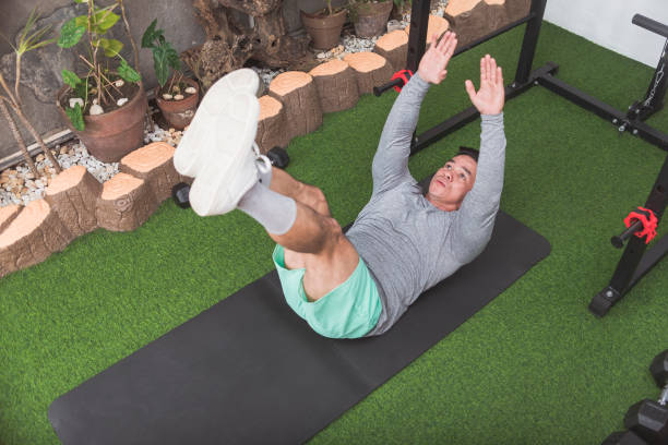 istock A fit asian man does V-ups with a plate while lying on a black mat. Arms and legs raised. Working out his core at his home gym. 2158547348